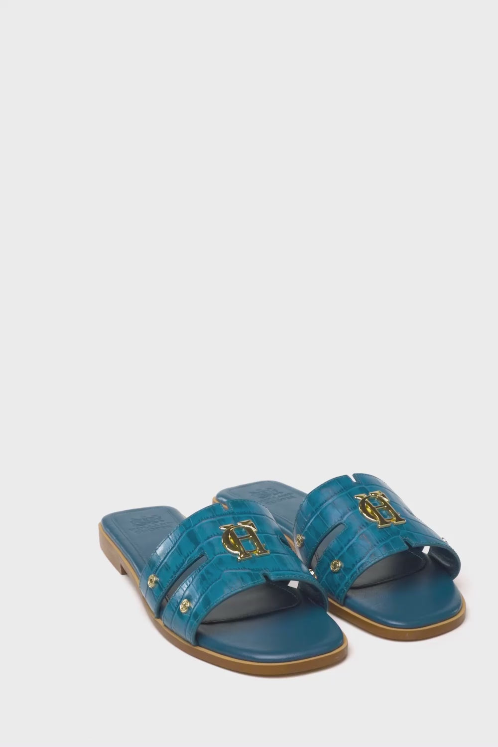 360 video of teal blue croc embossed leather sliders with  a tan leather sole and gold hardware.