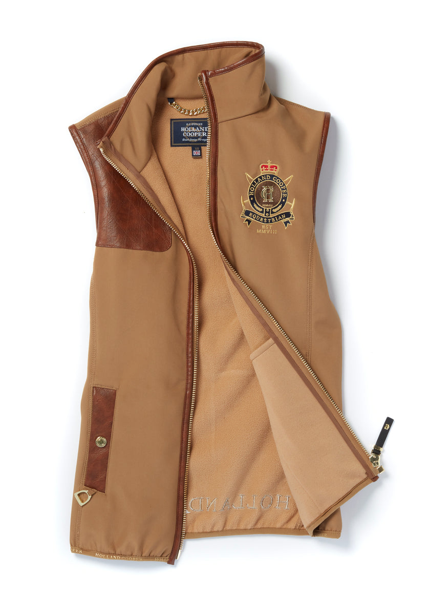 womens light brown gilet with dark brown leather seams along the arm holes pockets and down the zip with a gun patch on the shoulder and an embroidered logo