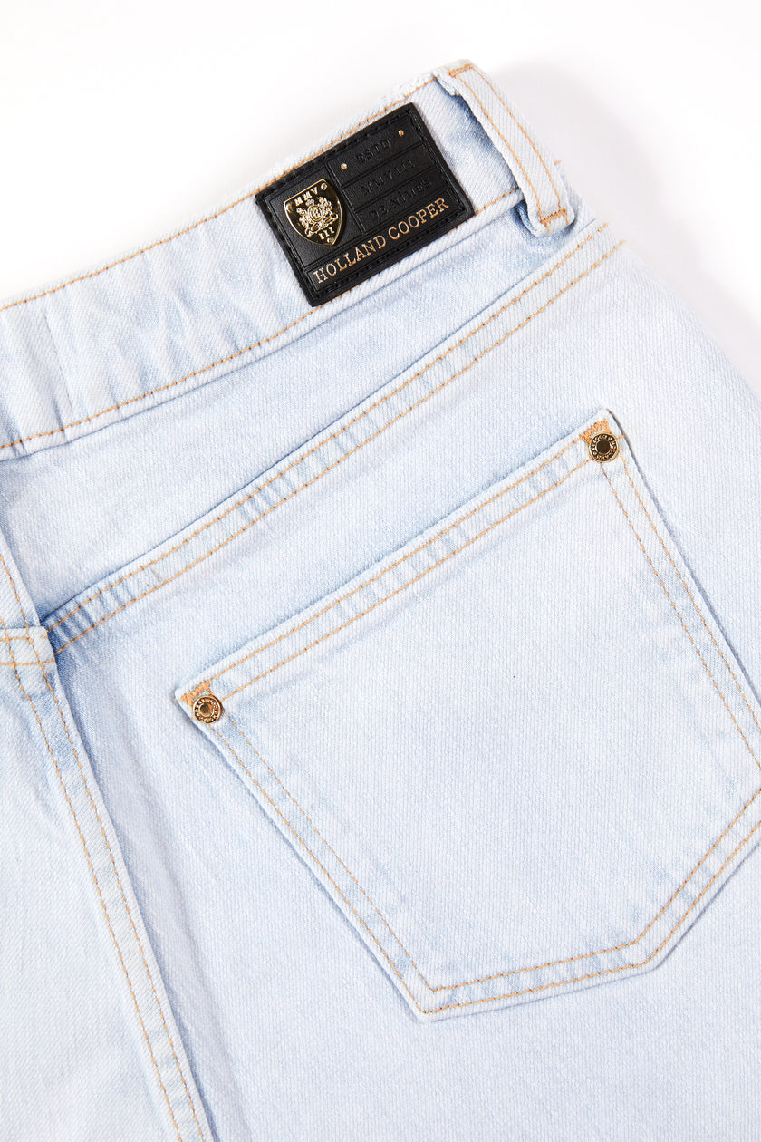 back pocket detail of womens light blue denim shorts with raw edge hemline and two open front pockets and two open back pockets with gold hc crest rivet in right front pocket